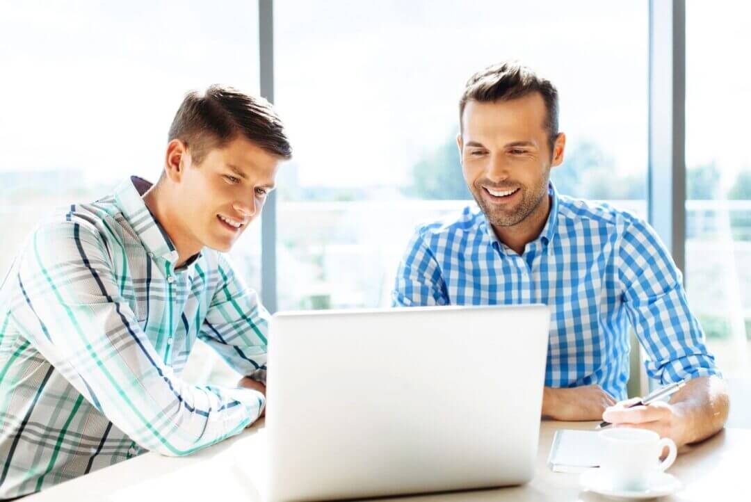 Deux hommes souriants devant un ordinateur portable au bureau